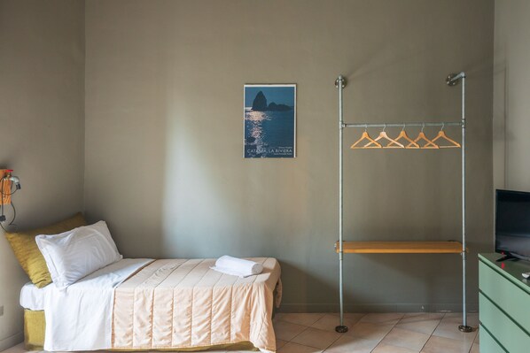 A bedroom with a bed, a hanging clothes rack, a poster on the wall, and a green dresser.