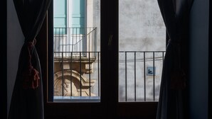 A window with curtains, a view of a building with a tiled roof, and a balcony railing. - Terrazza Santa Chiara (Catania)