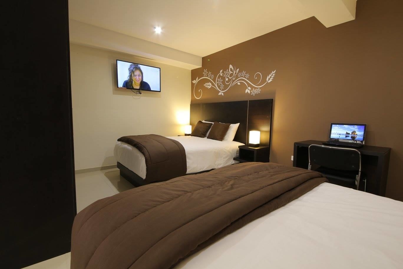 Una camera d'hotel con un letto, una scrivania con un portatile, una televisione a parete e un motivo decorativo.