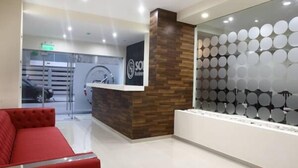Un área de recepción con diseño moderno, que incluye una pared de acento de madera, un mostrador de recepción y una zona de estar con un sofá rojo.
