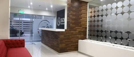 Un área de recepción con diseño moderno, que incluye una pared de acento de madera, un mostrador de recepción y una zona de estar con un sofá rojo.