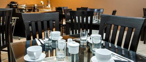 A dining area with glass tables, black chairs, and white tableware.