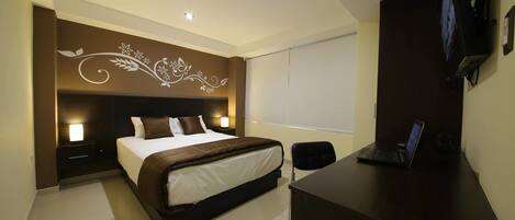 A modern hotel room with a large bed, a desk with a laptop, a flat-screen TV, and a decorative wall design.