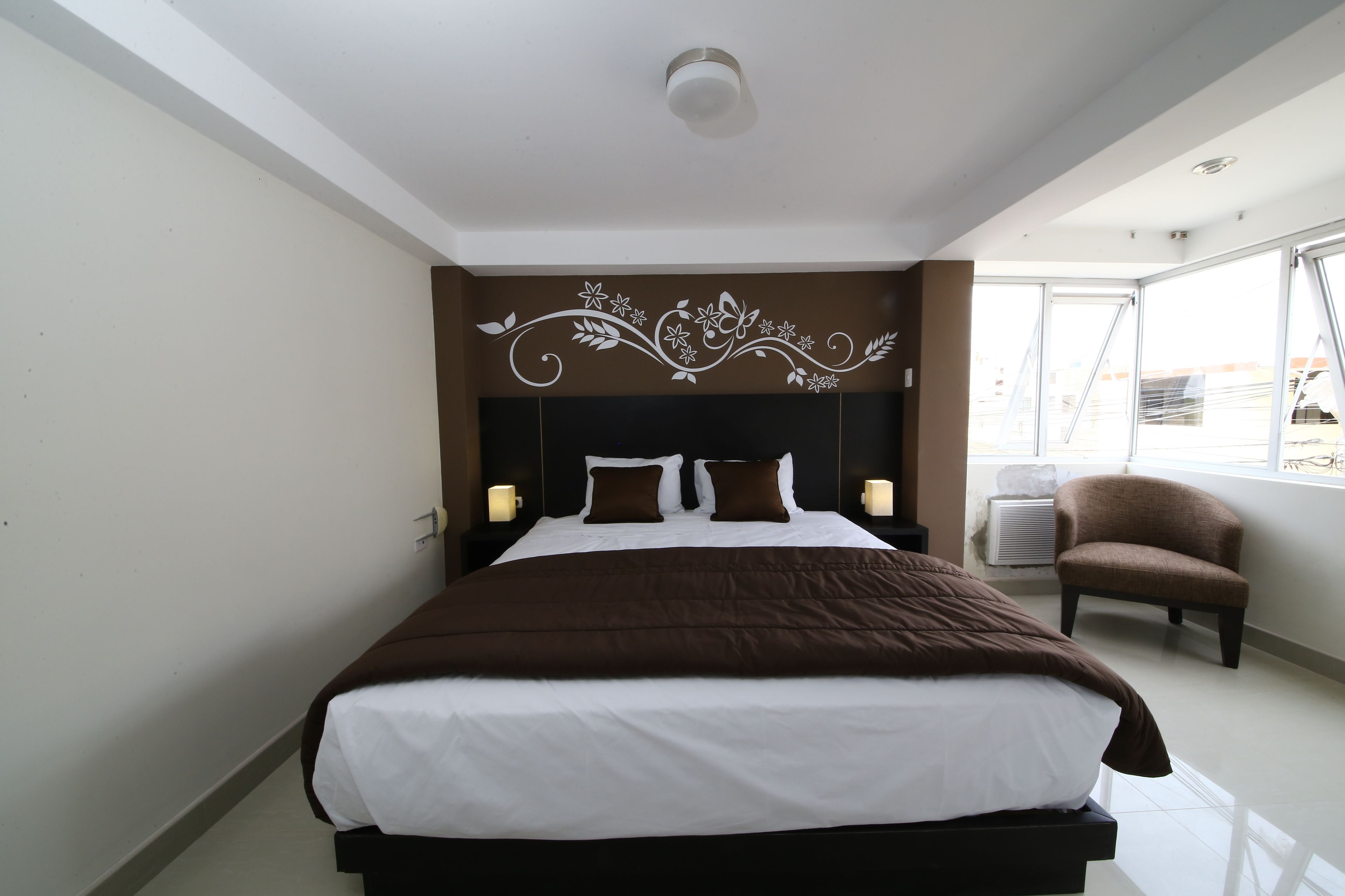 Una habitación de hotel con una cama grande, una silla, un detalle decorativo en la pared y una ventana.