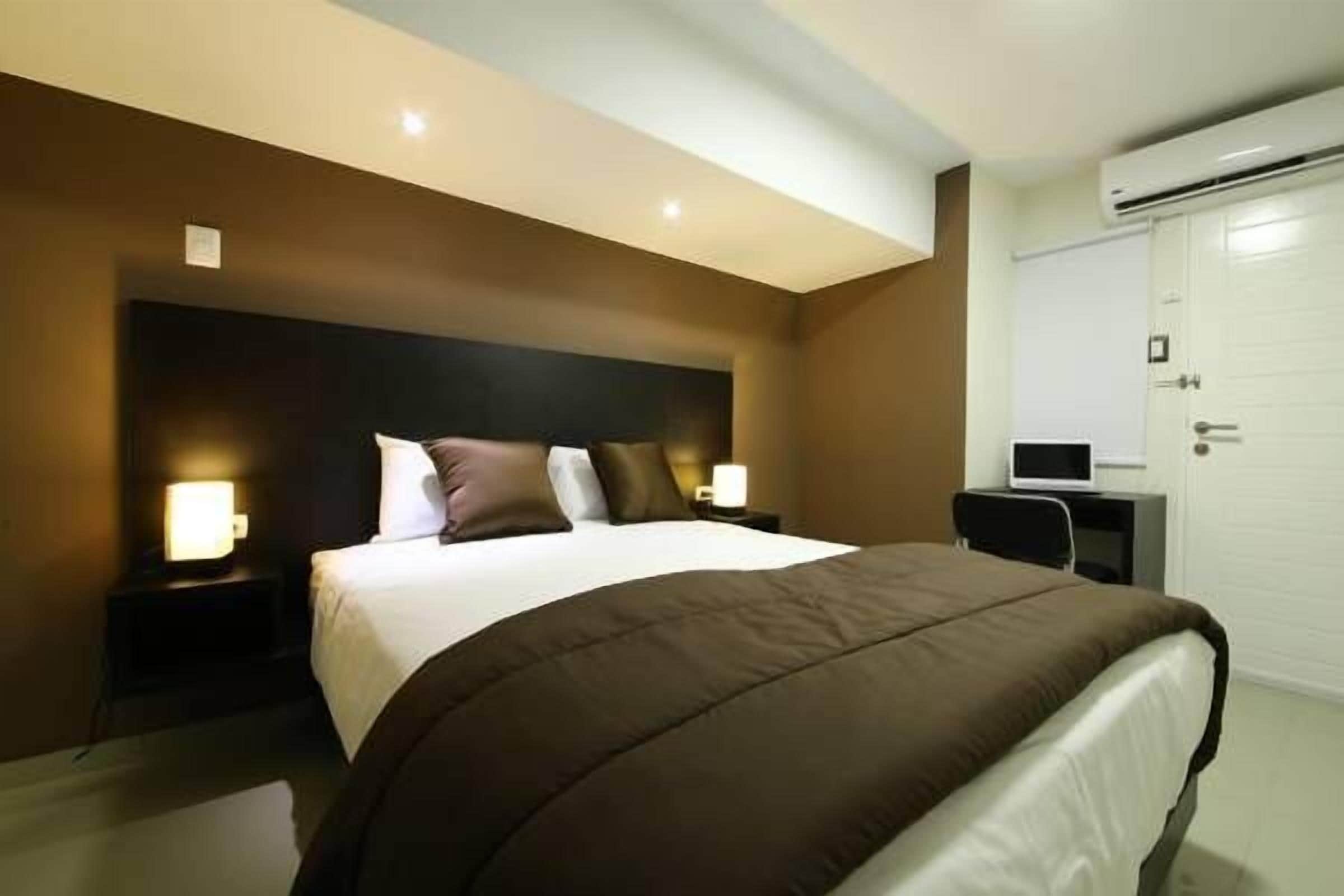 Una habitación de hotel moderna con una cama grande, lámparas de noche, un escritorio y un armario.
