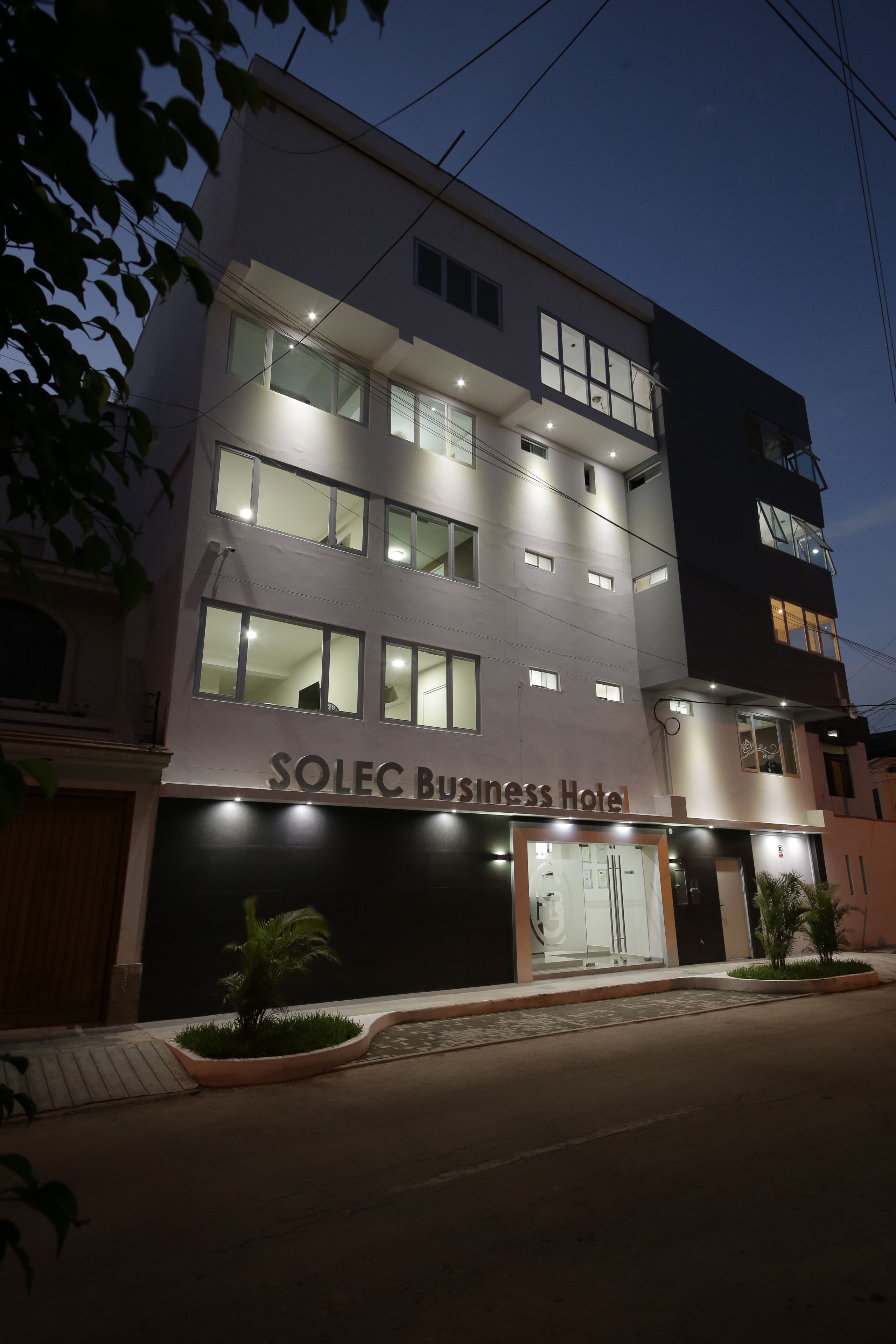 Un edificio moderno con un letrero que dice "SOLEC Business Hotel". Tiene varios pisos con grandes ventanales y una entrada bien iluminada.