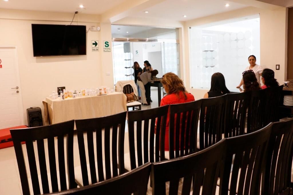 Un salón de conferencias con una mesa blanca, sillas negras y un televisor en la pared.