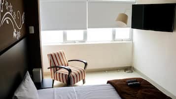Habitación de hotel con cama, una silla, un televisor y un ventanal con persianas.