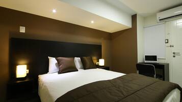 A hotel room with a large bed, bedside lamps, a desk with a laptop, and an air conditioning unit.
