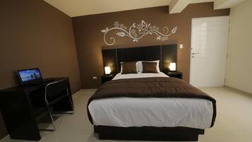 A bedroom with a large bed, a desk with a laptop, and a door.