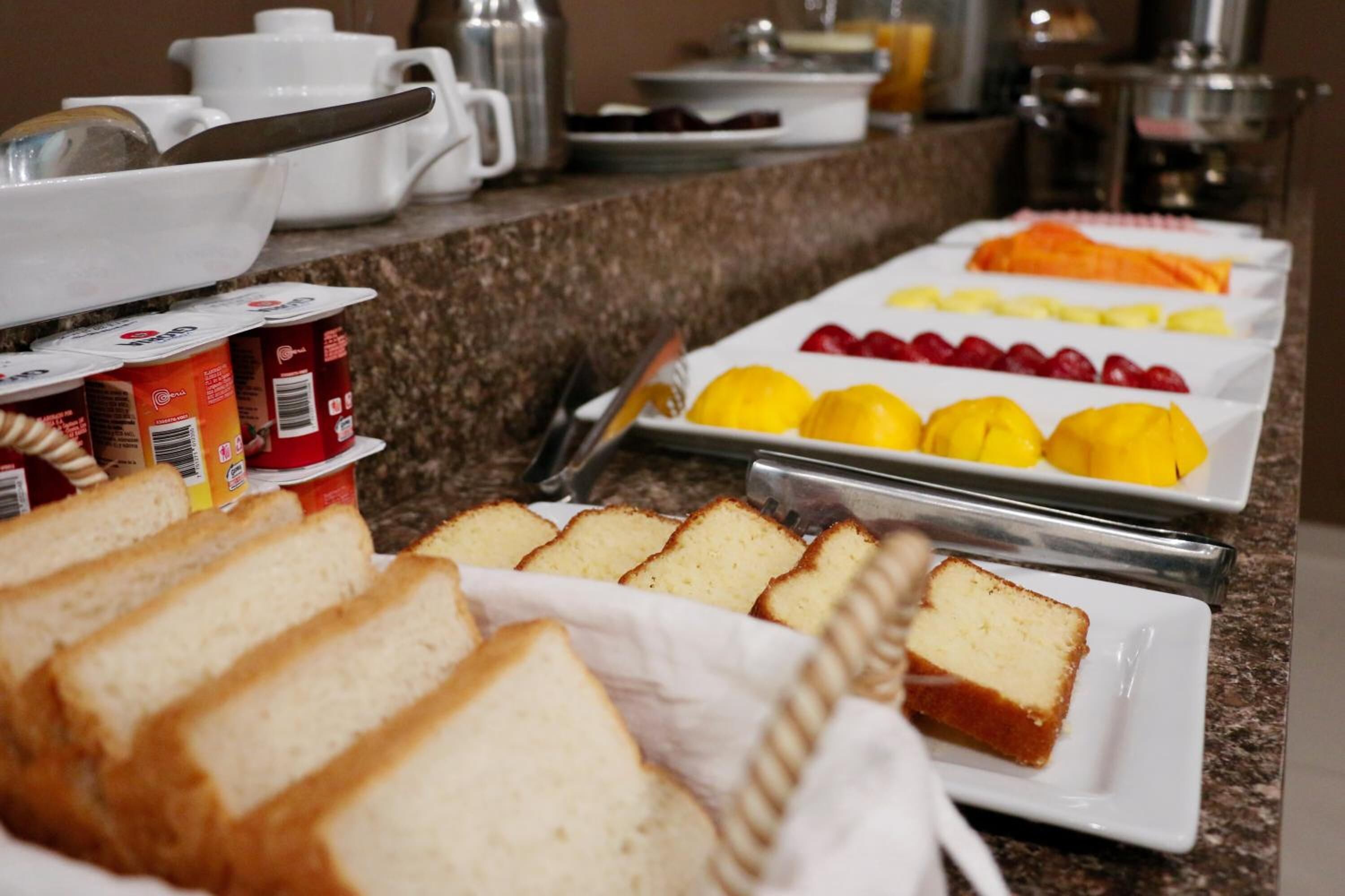 A breakfast buffet with bread, fruits, and beverages.