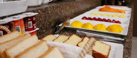 A breakfast buffet with bread, fruits, and beverages.