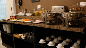 Montaje de bufé con diversos platos, una máquina de café y una selección de tazas y cuencos en estantes.