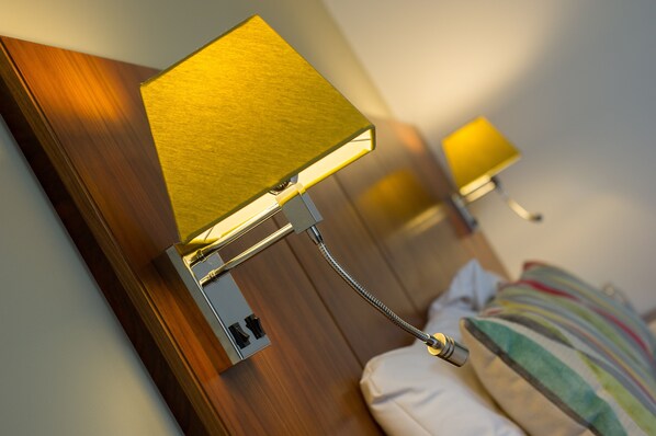 A close-up of a wall-mounted lamp with a metallic base and a golden shade, positioned above a bed with a striped pillow.