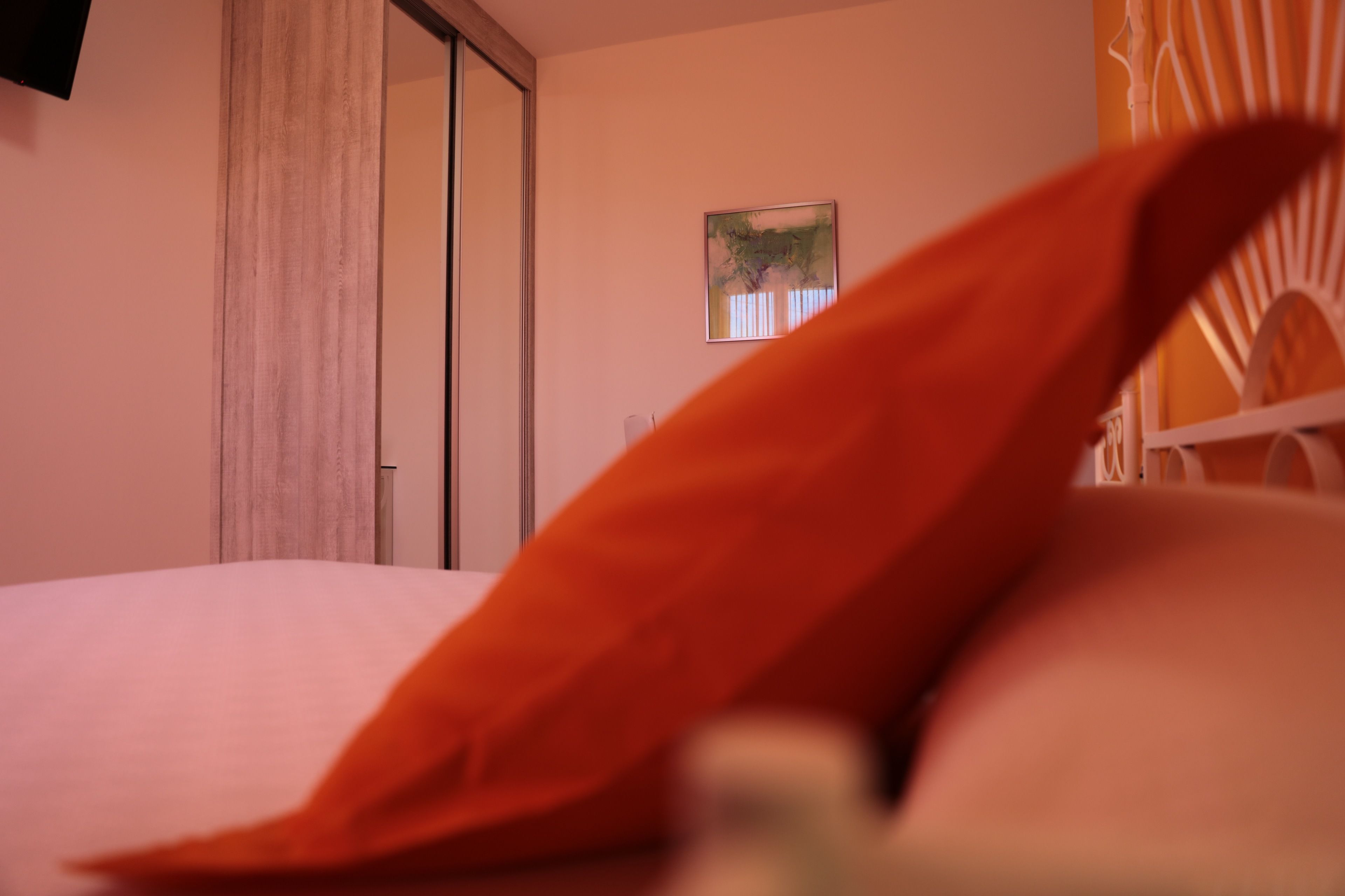 A hotel room with a bed, a window with curtains, a painting on the wall, and a white chair.