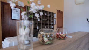Un mostrador de recepción con encimera de madera, un florero de vidrio con flores blancas y un cuenco de vidrio con caramelos de colores.