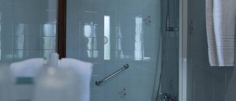 Un baño con cabina de ducha de vidrio, una barra de apoyo y una toalla blanca colgada en la pared.