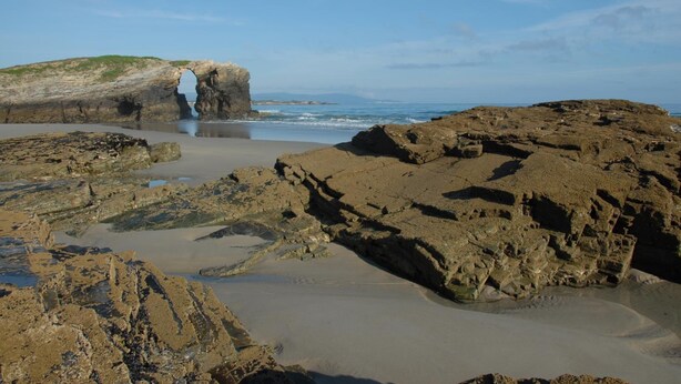 Una playa rocosa con una formación natural en arco y una vista despejada del océano.
