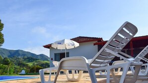 Area piscina con lettini e un ombrellone con marchio Visa, con vista sulle montagne e su un cielo sereno.