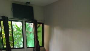 Une chambre à coucher avec un lit, une chaise, une fenêtre avec des rideaux et une petite table sur laquelle est posée une fleur.