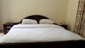 A neatly made bed with white bedding, two bedside tables with lamps, and a plain wall with a power outlet. - AES Luxury Apartments (Lagos)