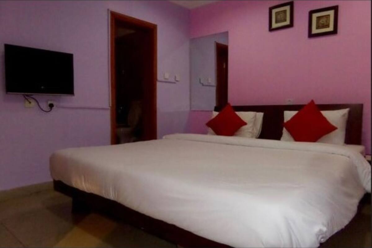 A bedroom with a bed, a television mounted on the wall, and a door leading to another room.