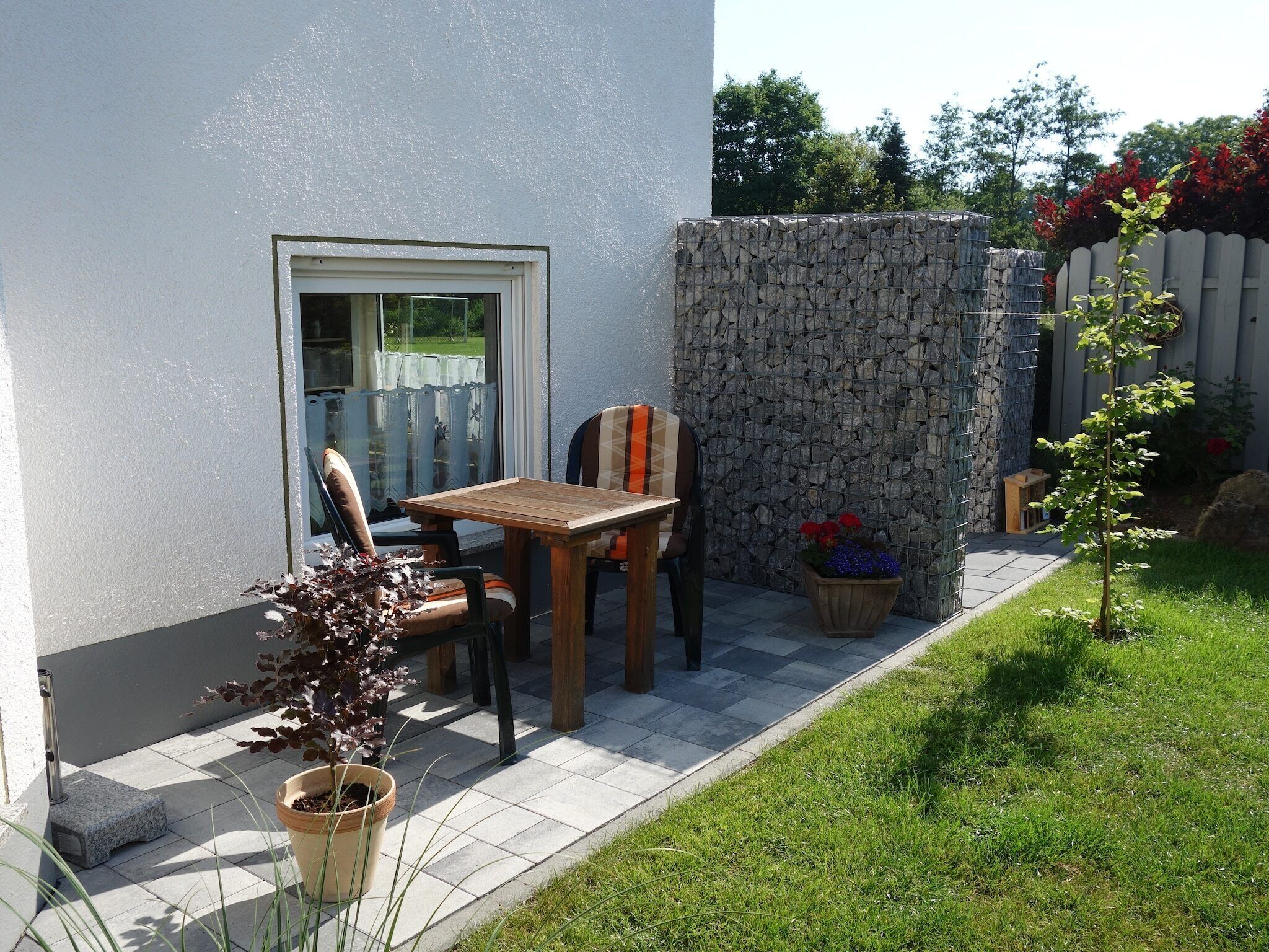 Eine Terrasse mit Tisch und Stühlen, einem Blumentopf und einer Steinmauer.