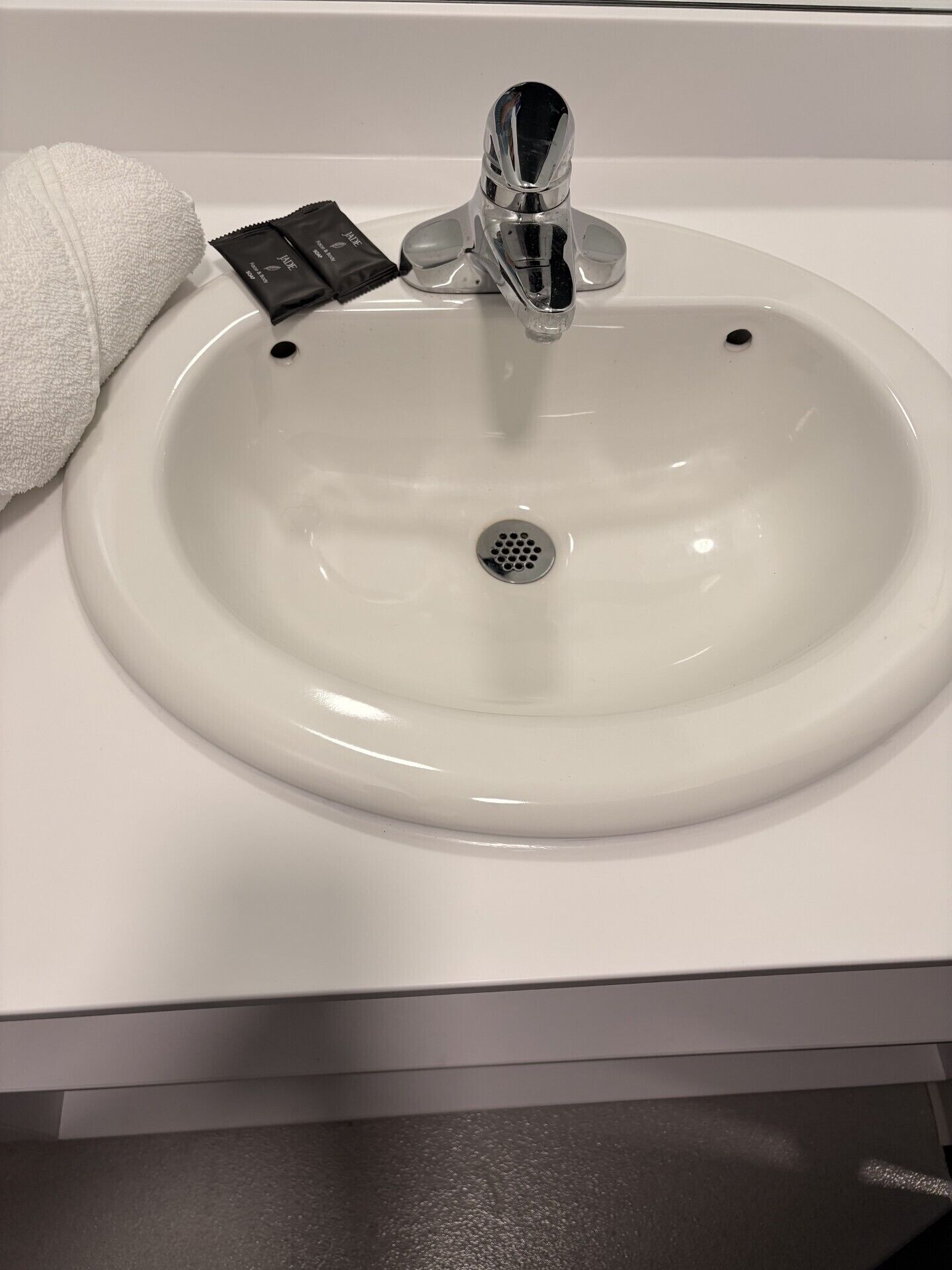 Un lavamanos blanco con grifo cromado, una toalla y dispensador de jabón.