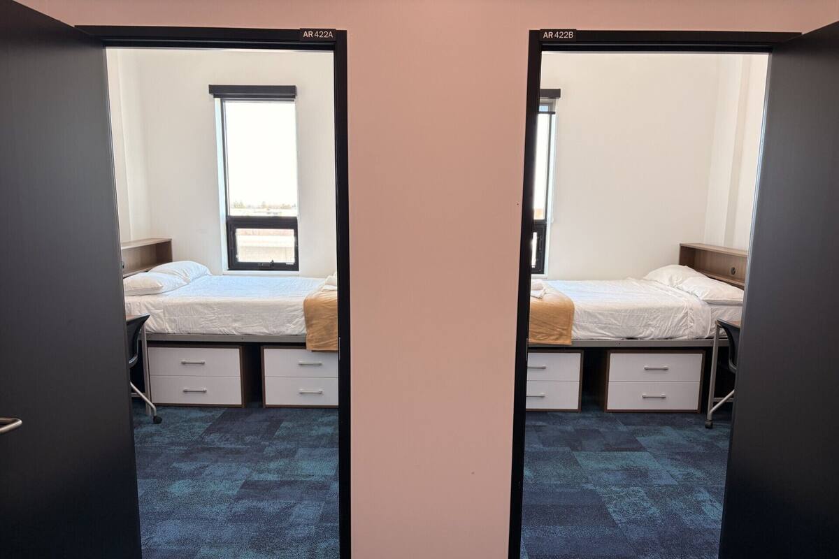A mirrored room with two beds, a window, and a carpeted floor.