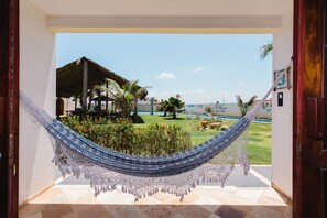 A hammock in a doorway overlooking a pool and a thatched-roof structure. - Pousada Blauset (São Gonçalo do Amarante)