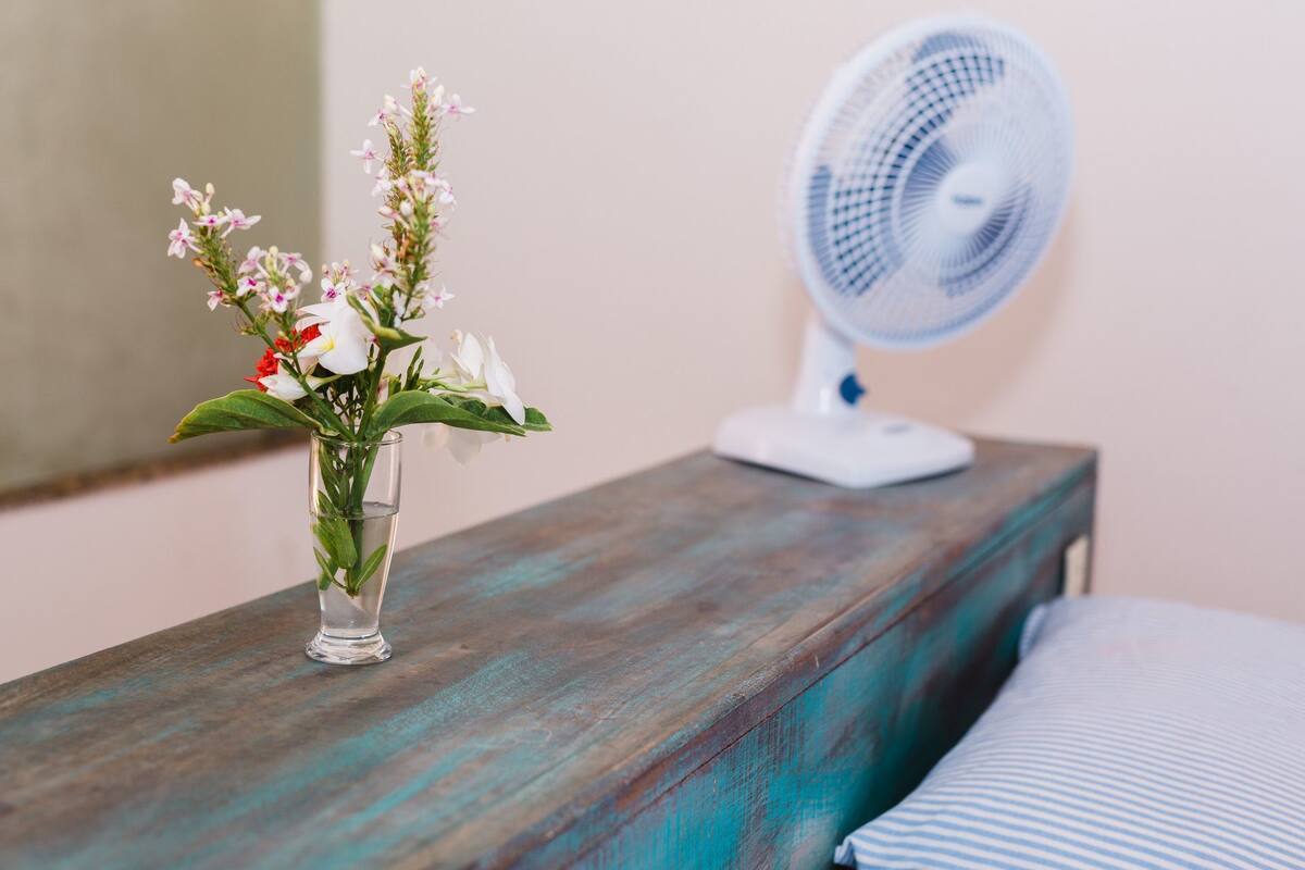 Ein Nachttisch aus Holz mit einem weißen Ventilator und einer Glasvase mit Blumen.