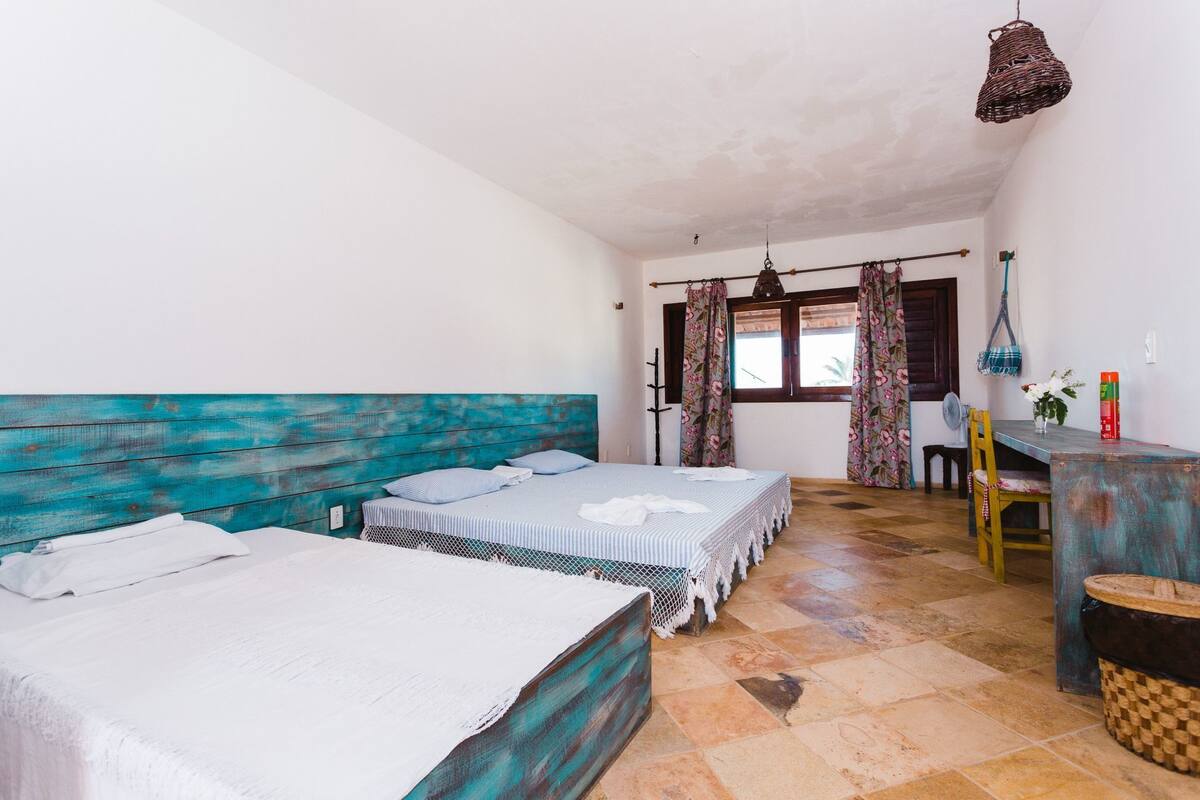 Ein Zimmer mit zwei Betten, einem hölzernen Kopfteil, einem Schreibtisch mit Stuhl, einer Pendelleuchte und einem Fenster mit Vorhängen.