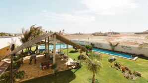 Zona de piscina con estructura de techo de paja, sillas de descanso y vista a la playa.
