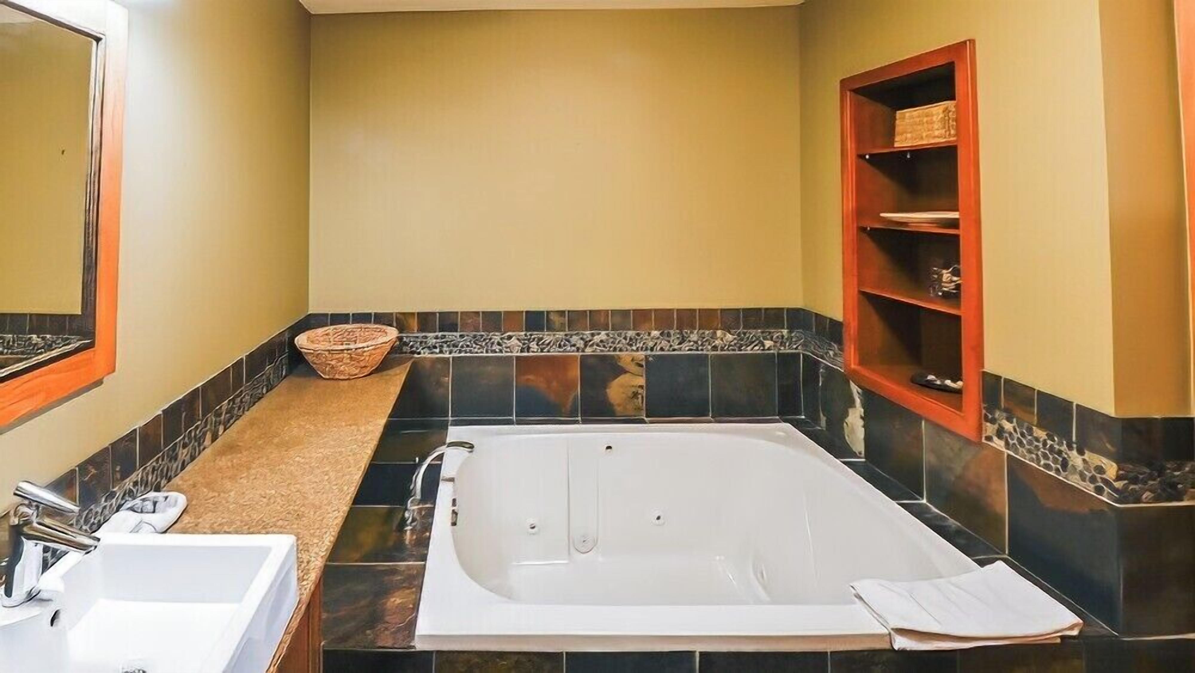 A bathroom with a bathtub, a sink, a mirror, and a shelf with toiletries.
