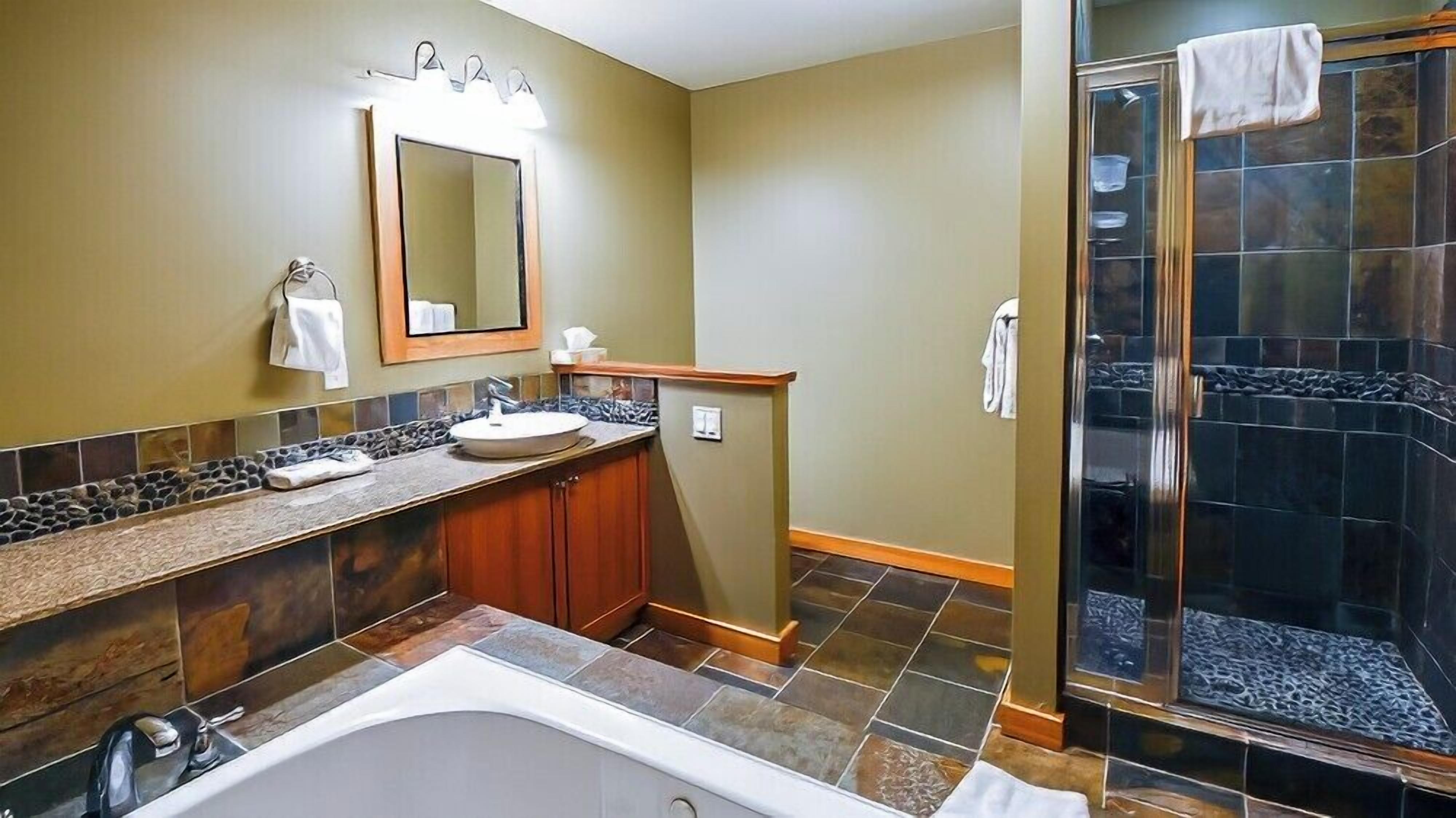 A bathroom with a bathtub, a sink with a vanity, a mirror, and a shower area.