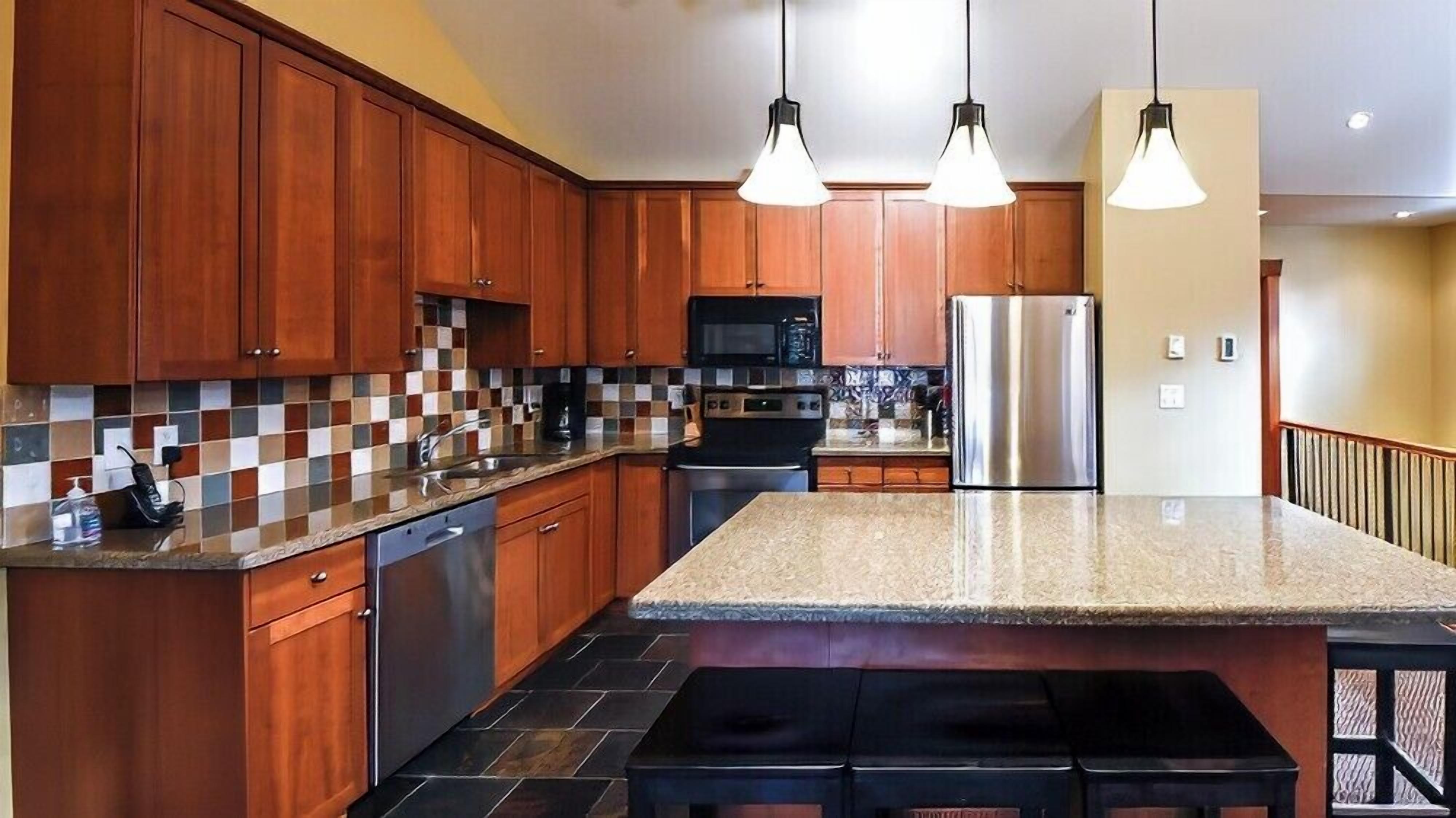A kitchen with wooden cabinets, a granite countertop, a stainless steel refrigerator, and a microwave.
