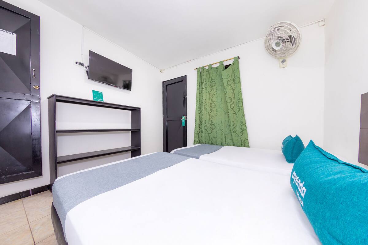 Ein Hotelzimmer mit Bett, Schreibtisch, Fernseher, Ventilator und einem grünen Vorhang.