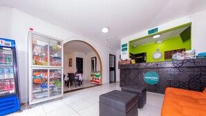 A hotel reception area with a vending machine, a glass display case, a reception desk, and a seating area with two ottomans and an orange couch. - Ayenda Villas de San Juan (Medellín)