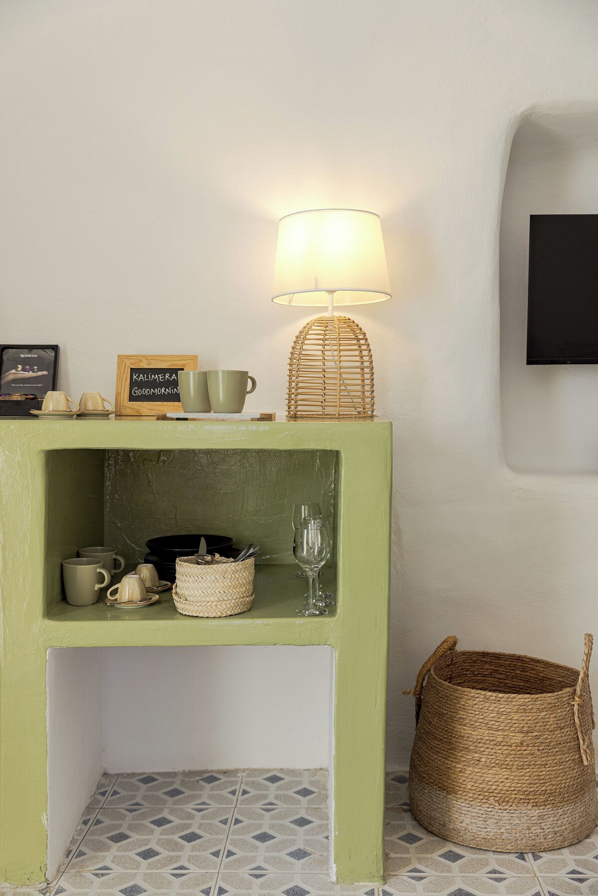 Een groene plank met een geweven lamp, een lijst en verschillende bekers en een wijnglas.
