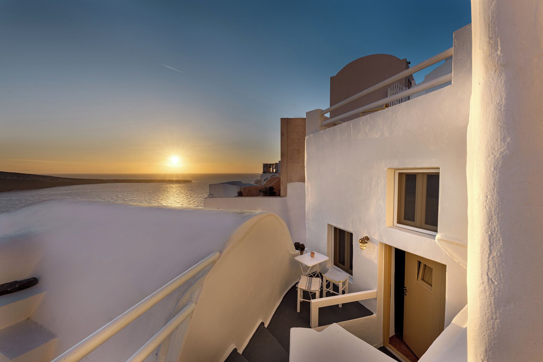 Un edificio blanco con balcón que da al mar al atardecer.