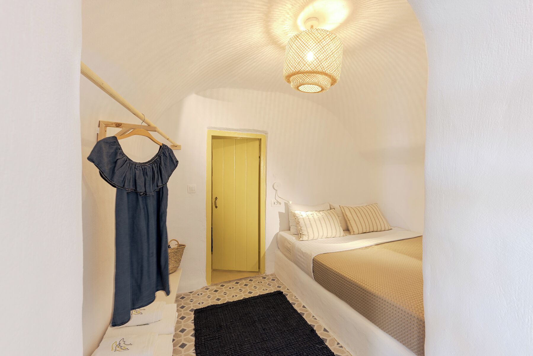Un dormitorio con cama, lámpara colgante, una puerta y un perchero de pared con ropa.