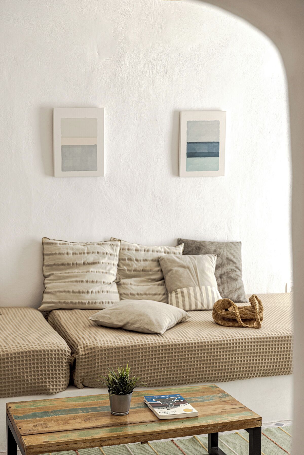Un salon moderne avec un canapé, des coussins, une table basse, une plante et deux œuvres d’art encadrées accrochées au mur.