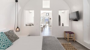 A bedroom with a bed, a TV, a stool, and a view through an arched doorway. - Just Blue (Santorini)
