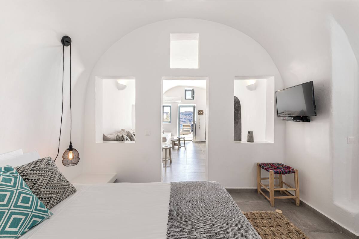 Un dormitorio con cama, televisor, taburete y vistas a través de un arco.