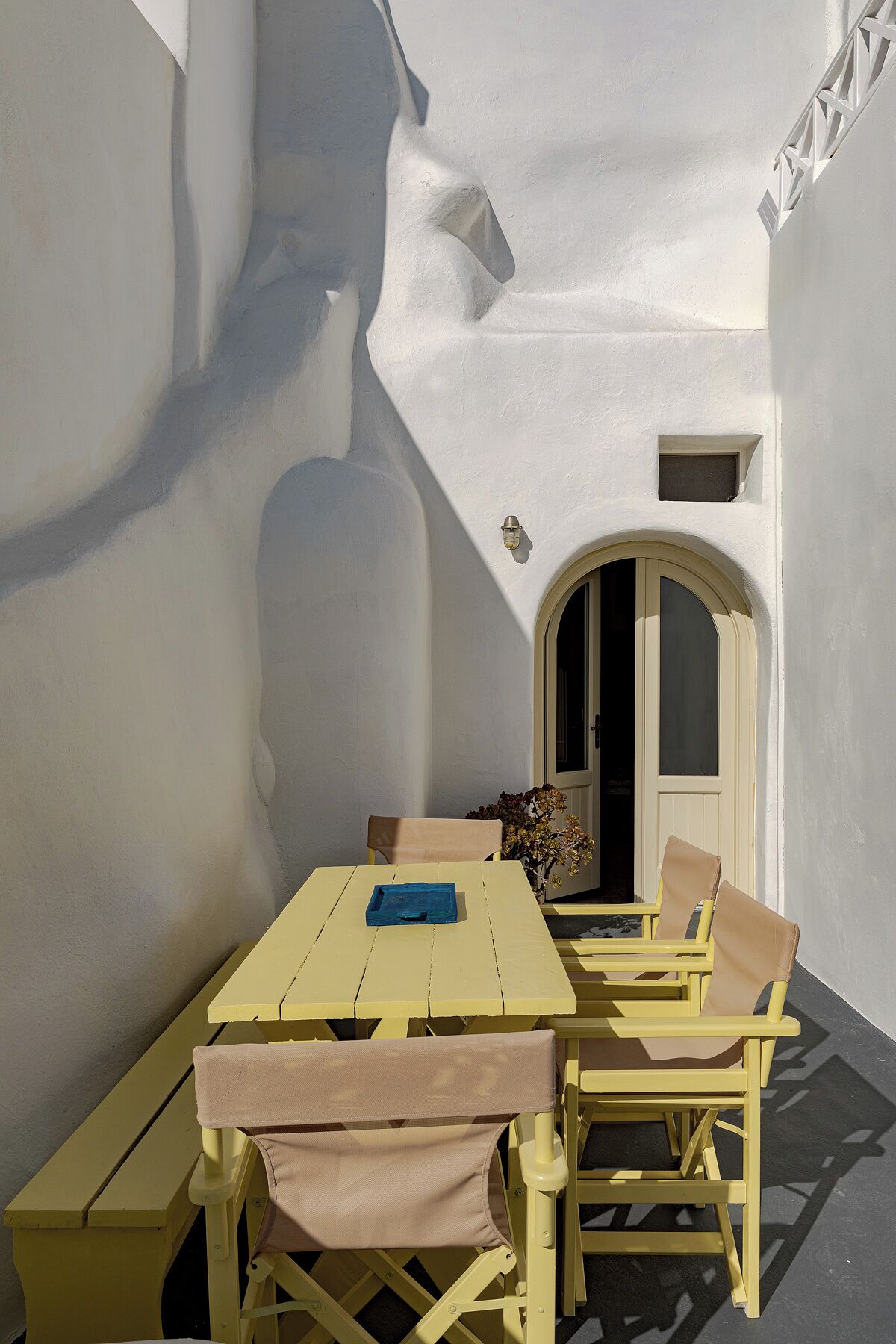 A sunlit outdoor seating area with a table and chairs, a small window, and a door.
