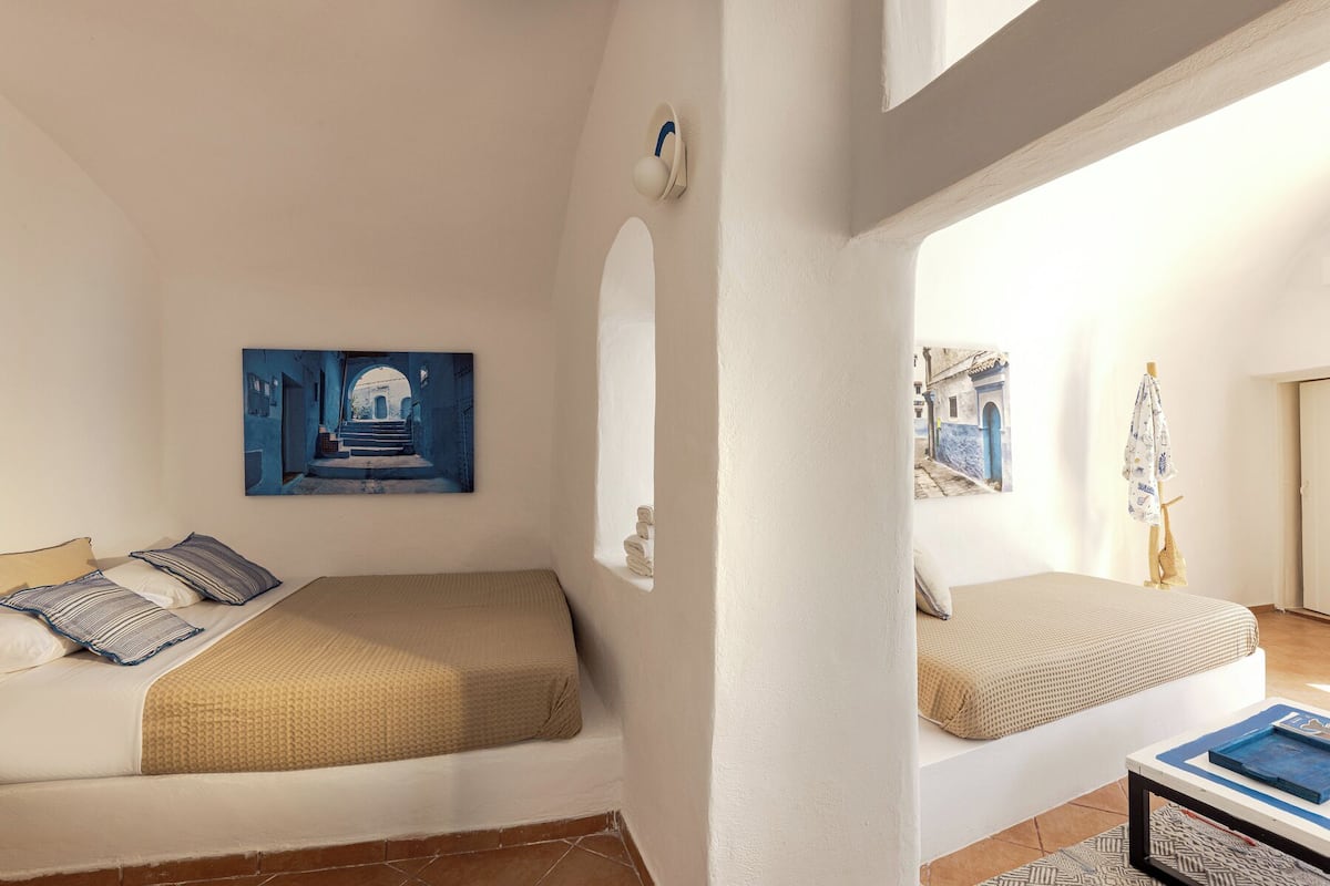 Una habitación con una cama, una mesita y una pared con dos cuadros enmarcados.