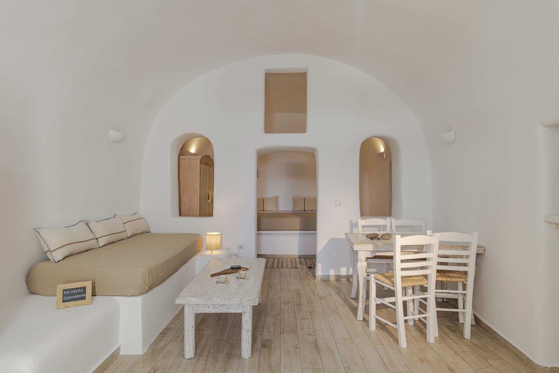 A minimalist room with a sofa, a table, and chairs, an arched doorway, and a mirror.