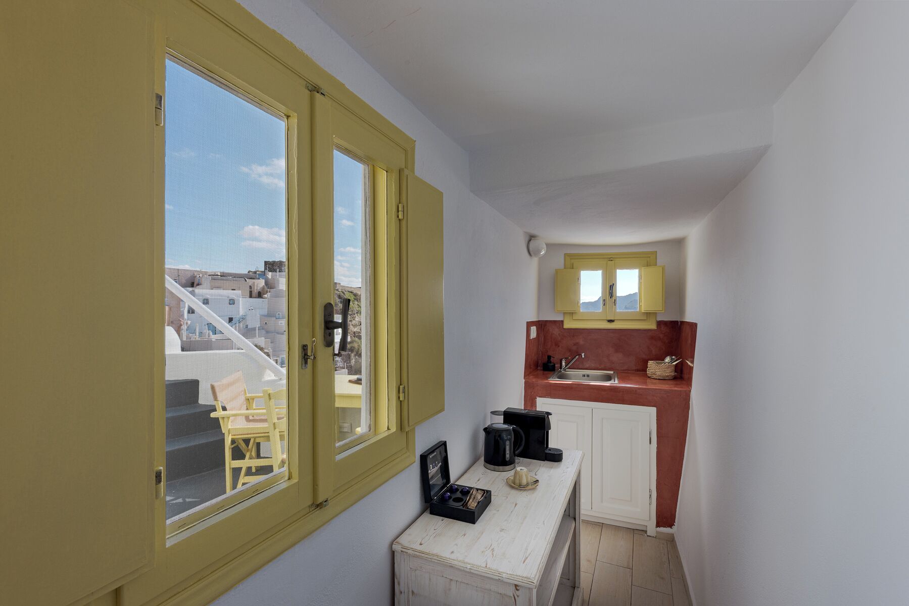 Cocina compacta con ventana, un lavamanos y una pequeña mesa con tetera y tazas.