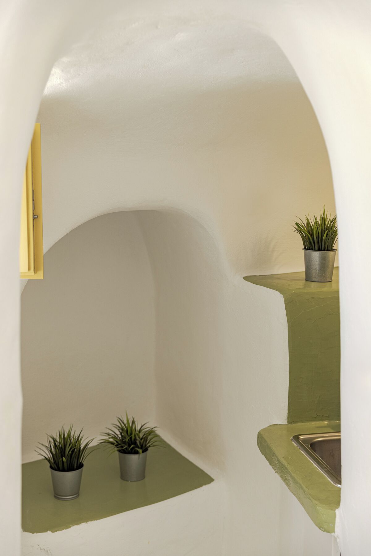 Una petita alcova arrodonida amb un finestret, dues plantes en testos i un lavabo.