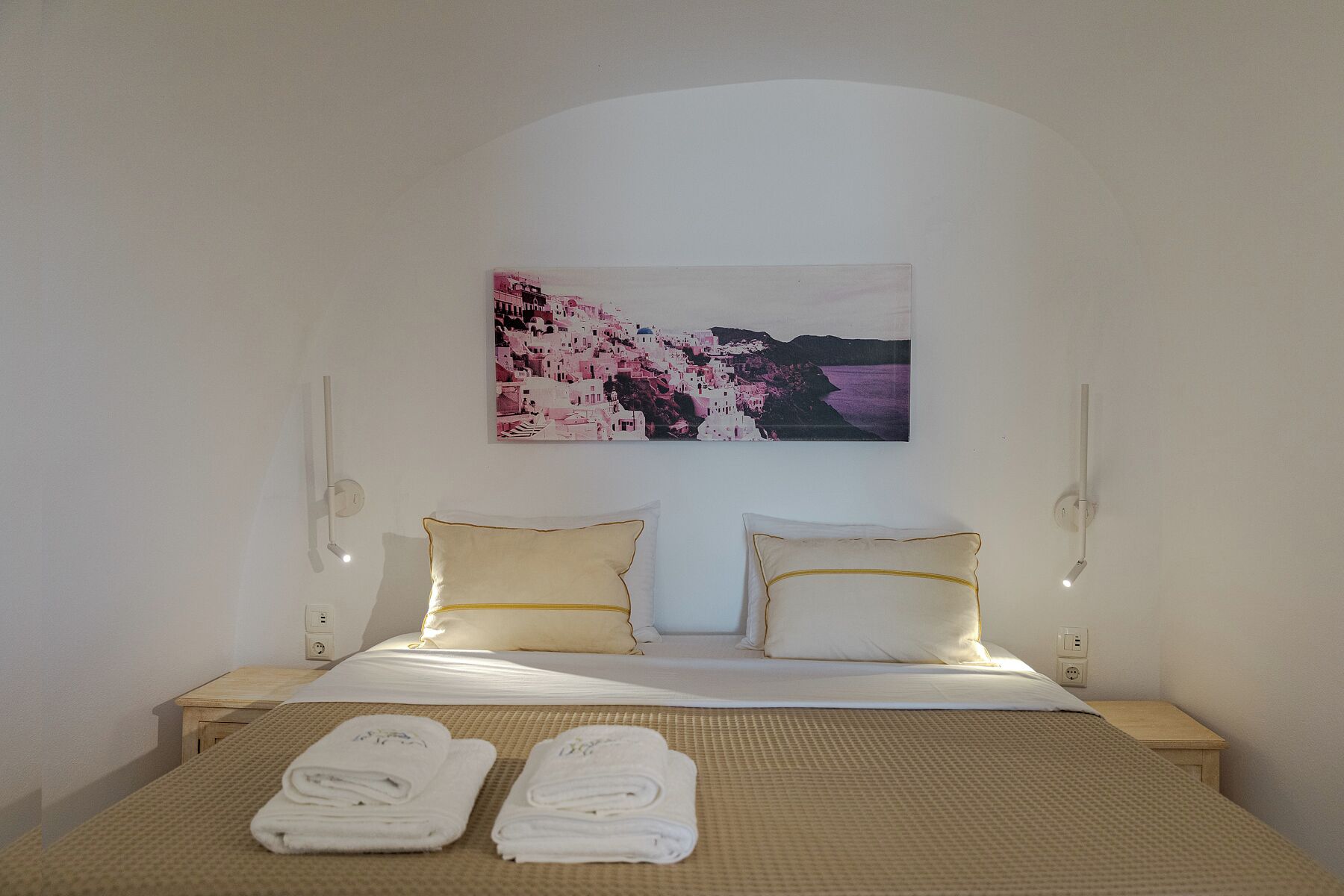 Une chambre d’hôtel avec un lit, deux oreillers, un tableau accroché au mur, des lampes de chevet et deux serviettes roulées posées sur le lit.